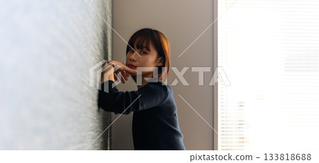 A Japanese woman with short hair leaning against a wall and looking at the camera 133818688