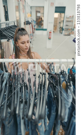 A young woman is shopping for jeans in a trendy retail store that sells fashionable apparel A young woman is shopping for jeans in a trendy retail store that sells fashionable apparel 133818798