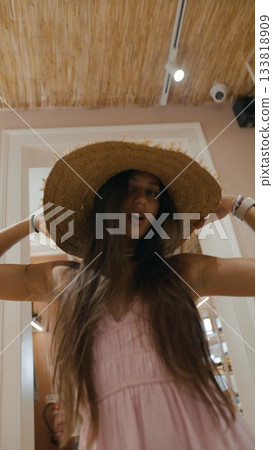 A Young Woman Adorned in a Straw Hat, Joyfully Posing and Playfully Expressing Indoors A Young Woman Adorned in a Straw Hat, Joyfully Posing and Playfully Expressing Indoors 133818909