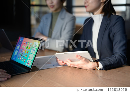 Businesswomen having a meeting in a conference room using a tablet and laptop Businesswomen having a meeting in a conference room using a tablet and laptop 133818956