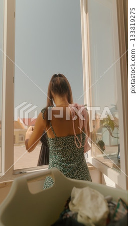 A Woman is Delighting in the Warmth of a Beautiful Sunny Day by the Window at Her Home 133819275
