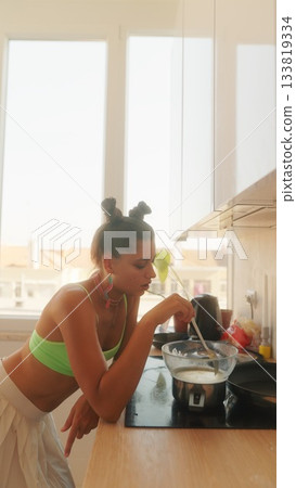 A Young Woman Engaged in Cooking Activities within a Modern Kitchen Bathed in Natural Light A Young Woman Engaged in Cooking Activities within a Modern Kitchen Bathed in Natural Light 133819334