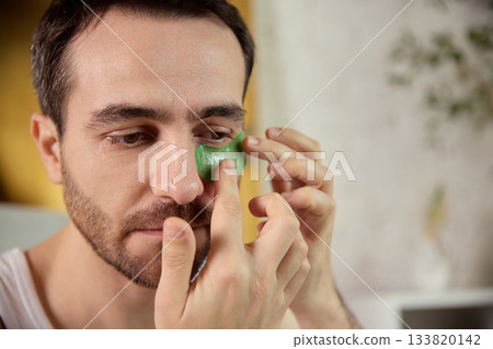 Man placing green under-eye patches for refreshing skincare treatment 133820142