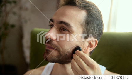 Man massaging beard line with gua sha tool in relaxed mood 133820152