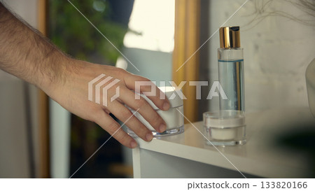Hand reaching for skincare cream on bathroom shelf. Hand reaching for skincare cream on bathroom shelf. 133820166