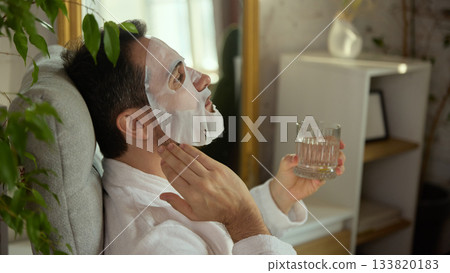 Man sitting with face mask and glass of water in peaceful moment Man sitting with face mask and glass of water in peaceful moment 133820183