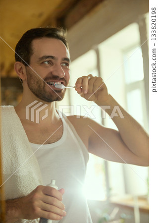 Man brushing teeth in bright morning bathroom light Man brushing teeth in bright morning bathroom light 133820198