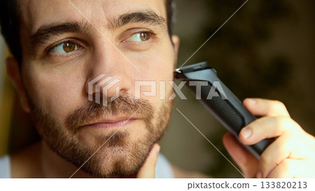 Man shaping beard line with trimmer in natural daylight Man shaping beard line with trimmer in natural daylight 133820213