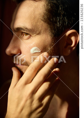 Man applying facial cream on cheek in natural light Man applying facial cream on cheek in natural light 133820236