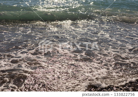 Gentle waves lapping the shore create a serene scene at the beach. Sunlight sparkles on the water, highlighting the beauty of this natural escape 133822756
