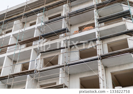 Workers are using scaffolding to access different levels of a multi-story building under construction. The image shows exposed walls and construction materials nearby 133822758