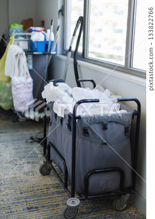 Cleaning staff prepare for guest turnover by collecting used linens and supplies from the hotel room. The service ensures a tidy and welcoming environment for visitors 133822766