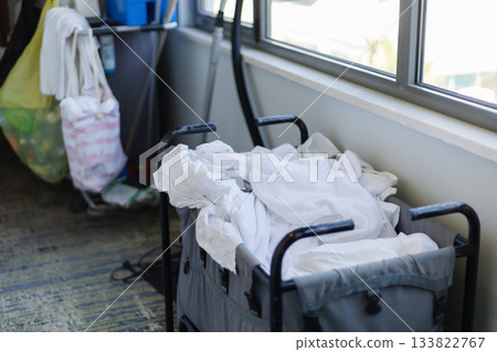 Housekeeping staff organizes clean white linens in a cart within a hotel room. The room features large windows letting in natural light, creating a neat environment 133822767