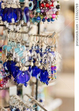 A decorative stand showcases various pieces of colorful jewelry in a lively market. The sparkling blues and vibrant hues attract attention. Visitors explore the unique designs and materials 133822769