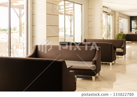 The seating area features stylish brown sofas arranged in a bright, spacious cafe. Large windows allow plenty of natural light to fill the room, creating an inviting atmosphere The seating area features stylish brown sofas arranged in a bright, spacious cafe. Large windows allow plenty of natural light to fill the room, creating an inviting atmosphere 133822780