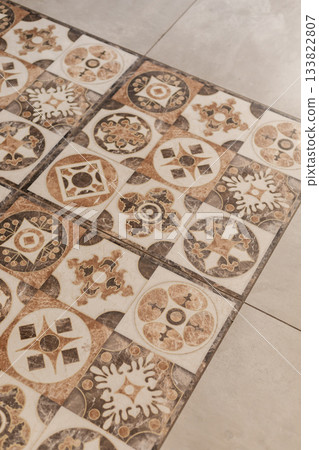 Decorative tiles with intricate patterns and earthy colors cover the floor of a well-lit indoor setting. The tiles enhance the aesthetic of the room, showcasing artistry and design 133822807