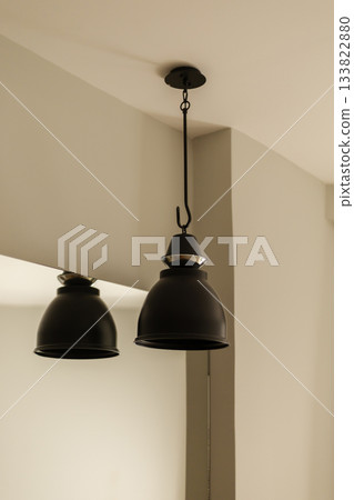 Two black pendant lights are suspended from the ceiling in a minimalistic setting, creating a cozy atmosphere. The design is simple yet elegant, enhancing the room's decor Two black pendant lights are suspended from the ceiling in a minimalistic setting, creating a cozy atmosphere. The design is simple yet elegant, enhancing the room's decor 133822880