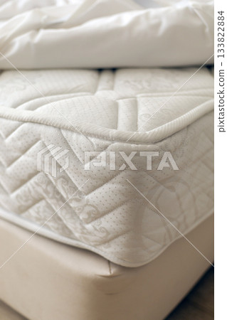 A plush mattress sits atop a soft bed frame, inviting relaxation. The soft bedding creates a warm and comfortable atmosphere, perfect for restful nights 133822884