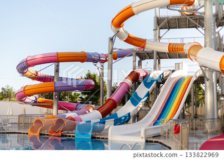 Brightly colored water slides twist and turn above a clear pool, inviting visitors to enjoy a fun day at the water park. The sky is cloudless and blue, enhancing the vibrant scene 133822969
