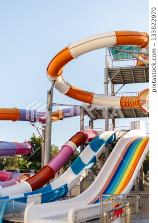 Brightly colored water slides spiral and twist under a clear blue sky, inviting visitors to enjoy thrilling rides at a family-friendly water park on a sunny afternoon 133822970
