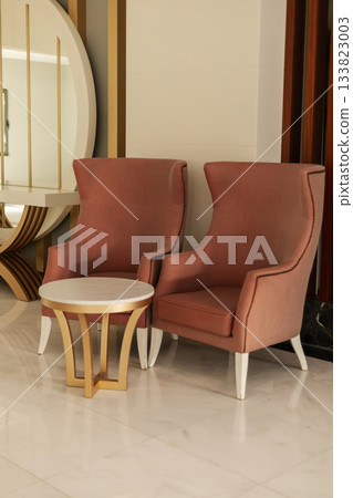 Two elegant pink chairs flank a round white table, creating a welcoming seating area. The modern decor features smooth lines and a bright atmosphere Two elegant pink chairs flank a round white table, creating a welcoming seating area. The modern decor features smooth lines and a bright atmosphere 133823003