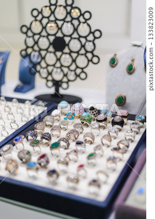 A colorful array of rings and earrings is showcased on a table at a jewelry shop, with bright gems and intricate designs attracting buyers during a busy market day A colorful array of rings and earrings is showcased on a table at a jewelry shop, with bright gems and intricate designs attracting buyers during a busy market day 133823009