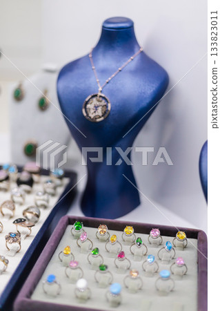 A collection of rings with various colored stones is displayed in a boutique. A necklace adds elegance to the setup, highlighting creative jewelry designs A collection of rings with various colored stones is displayed in a boutique. A necklace adds elegance to the setup, highlighting creative jewelry designs 133823011
