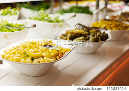 A vibrant buffet spread showcases bowls of pasta, lettuce, and pickles. The bright colors and textures invite guests to create their own delicious meal 133823024