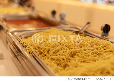 Multiple trays display different types of noodles prepared for a buffet. The bright setting enhances the inviting atmosphere, making it perfect for lunchtime gatherings 133823025