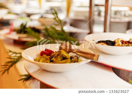 A selection of colorful appetizers is displayed in white bowls on a buffet table. The setting is bright and inviting, perfect for a lively lunch gathering 133823027