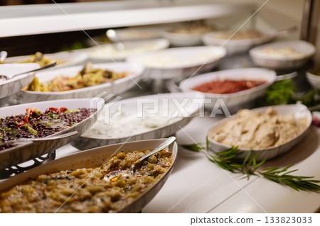 A variety of dishes are beautifully arranged in white bowls on a buffet table, showcasing a feast of colors and flavors. Guests enjoy the inviting atmosphere A variety of dishes are beautifully arranged in white bowls on a buffet table, showcasing a feast of colors and flavors. Guests enjoy the inviting atmosphere 133823033