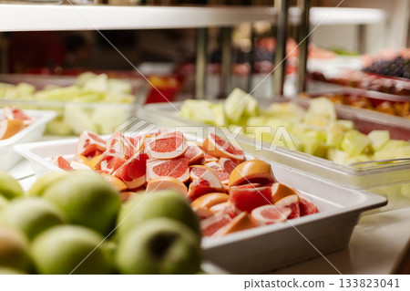 A colorful assortment of sliced and whole fruits is arranged neatly in a buffet setting. This vibrant spread includes melons, apples, and citrus. Perfect for an evening gathering or party A colorful assortment of sliced and whole fruits is arranged neatly in a buffet setting. This vibrant spread includes melons, apples, and citrus. Perfect for an evening gathering or party 133823041