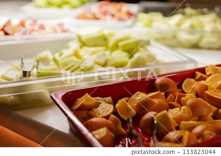 A vibrant selection of fresh fruits is arranged beautifully at a buffet, featuring orange slices, melons, and citrus fruits. The display invites guests to taste healthy options A vibrant selection of fresh fruits is arranged beautifully at a buffet, featuring orange slices, melons, and citrus fruits. The display invites guests to taste healthy options 133823044