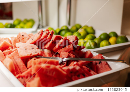 Colorful trays display neatly cut watermelon slices alongside vibrant green limes, perfect for refreshing snacks at a gathering or event during warm weather Colorful trays display neatly cut watermelon slices alongside vibrant green limes, perfect for refreshing snacks at a gathering or event during warm weather 133823045