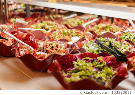 A vibrant salad bar is filled with an array of fresh vegetables and garnishes. The bowls showcase colorful ingredients, inviting guests to create their own healthy salads A vibrant salad bar is filled with an array of fresh vegetables and garnishes. The bowls showcase colorful ingredients, inviting guests to create their own healthy salads 133823051