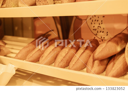 Soft, golden loaves of bread are neatly arranged on a wooden shelf in a charming bakery. The warm atmosphere invites customers to enjoy fresh baked goods Soft, golden loaves of bread are neatly arranged on a wooden shelf in a charming bakery. The warm atmosphere invites customers to enjoy fresh baked goods 133823052