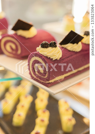 Beautifully decorated purple roll cakes topped with cream and chocolate sit invitingly on a dessert display, attracting attention at a festive gathering 133823064