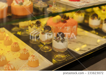 A variety of colorful desserts are neatly arranged in a glass display case. Soft textures and vibrant colors attract attention, making it hard to choose a favorite treat 133823072
