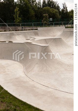 A modern skatepark features smooth, flowing concrete structures with various ramps and bowls, ideal for skateboarding and BMX activities. The park is surrounded by green trees and is well-maintained A modern skatepark features smooth, flowing concrete structures with various ramps and bowls, ideal for skateboarding and BMX activities. The park is surrounded by green trees and is well-maintained 133823144