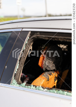 A car abandoned on the roadside shows signs of fire damage inside, with a burnt seat and shattered glass nearby, highlighting a scene of neglect or an accident A car abandoned on the roadside shows signs of fire damage inside, with a burnt seat and shattered glass nearby, highlighting a scene of neglect or an accident 133823150
