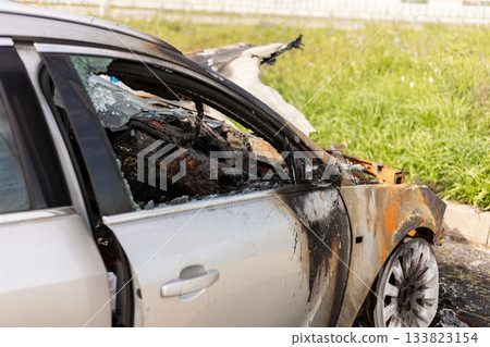 A car heavily damaged by fire is seen on the roadside. The metal is burnt and blackened, amidst green grass and remnants of the burnt vehicle, showing the aftermath of the incident A car heavily damaged by fire is seen on the roadside. The metal is burnt and blackened, amidst green grass and remnants of the burnt vehicle, showing the aftermath of the incident 133823154