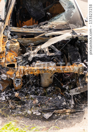 A car that caught fire is now a burnt shell, showing severe damage inside and out. The remnants of the engine and burnt materials are visible in a roadside setting 133823158