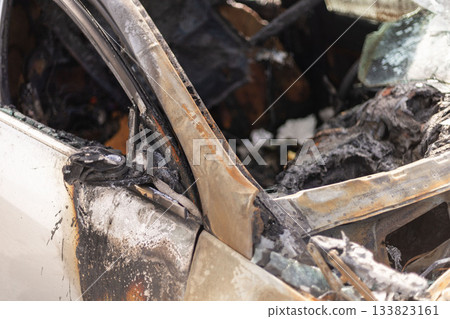 A burned car door reveals extensive fire damage in a parking lot. Charred materials and smoke residue surround the area, indicating a serious vehicle fire incident that occurred recently A burned car door reveals extensive fire damage in a parking lot. Charred materials and smoke residue surround the area, indicating a serious vehicle fire incident that occurred recently 133823161