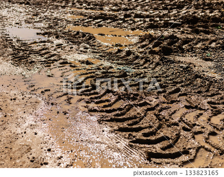 Tire tracks create intricate patterns in wet mud at a rural construction site. Puddles form in the low areas, reflecting the sky. The scene highlights the effects of rain on the terrain Tire tracks create intricate patterns in wet mud at a rural construction site. Puddles form in the low areas, reflecting the sky. The scene highlights the effects of rain on the terrain 133823165