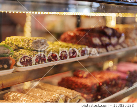 Shelves filled with an array of traditional sweets, featuring vibrant colors and textures. The display includes rolled desserts adorned with nuts and fruit, enticing customers 133823188