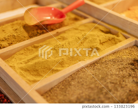 Brightly colored spices fill wooden trays at a local market. A red scoop sits in one of the spice compartments, inviting exploration of flavors and aromas Brightly colored spices fill wooden trays at a local market. A red scoop sits in one of the spice compartments, inviting exploration of flavors and aromas 133823196
