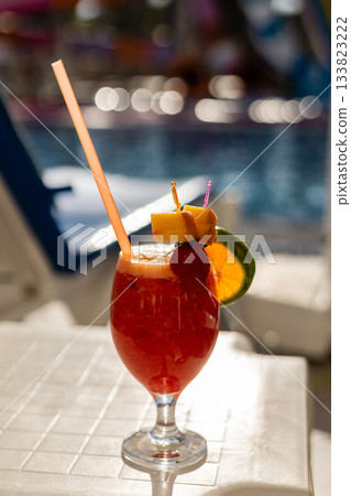 A vibrant tropical cocktail sits on a table by the poolside, featuring colorful garnishes like pineapple, orange, and cherries, perfect for a sunny day of relaxation A vibrant tropical cocktail sits on a table by the poolside, featuring colorful garnishes like pineapple, orange, and cherries, perfect for a sunny day of relaxation 133823222