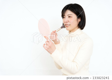 一位面帶微笑的女子正用手鏡化妝。 一位面帶微笑的女子正用手鏡化妝。 133823241