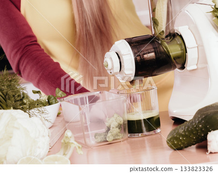 Woman in kitchen making vegetable smoothie juice 133823326
