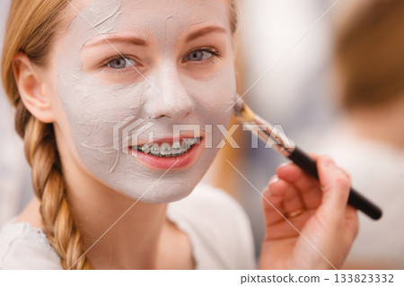 Woman applying with brush clay mud mask to her face Woman applying with brush clay mud mask to her face 133823332